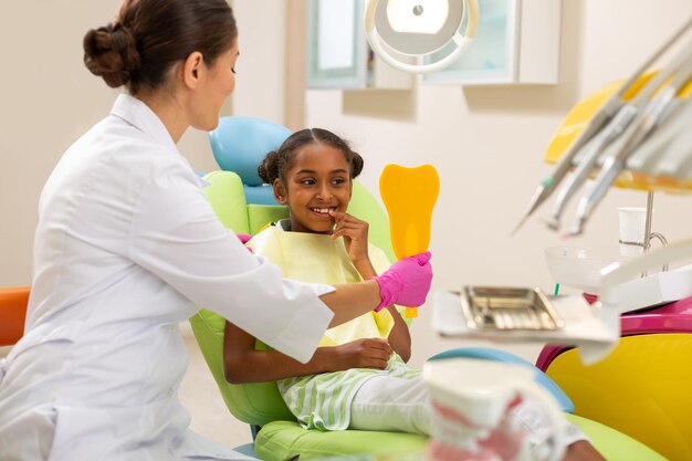 Dentista feminina segurando um espelho para uma garotinha