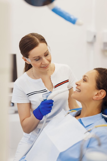 Dentista feminina sorridente examinando os dentes da mulher com instrumentos odontológicos no escritório moderno