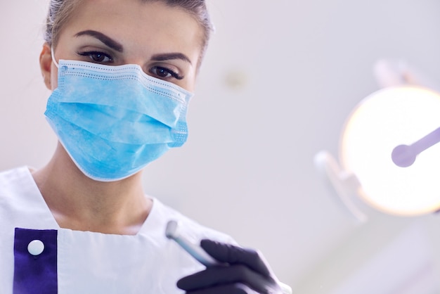 Dentista feminina tratando os dentes do paciente, close-up do rosto do médico na máscara