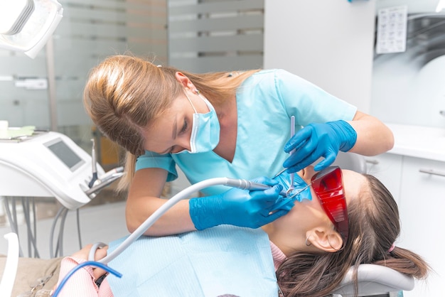Foto dentista feminina usando luvas está trabalhando na boca de uma jovem