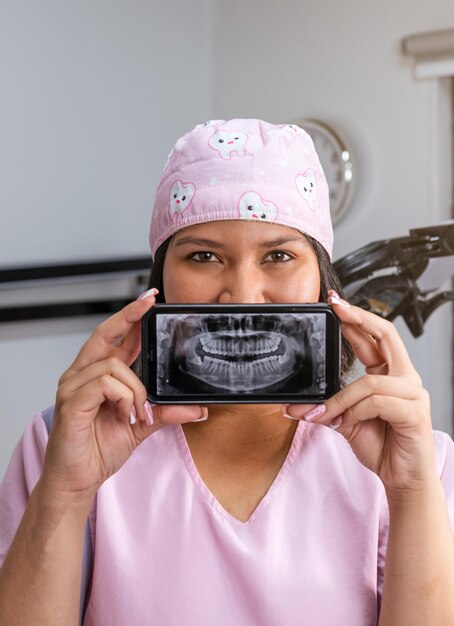 Dentista feminina usando smartphone para mostrar o raio X dental panorâmico do paciente