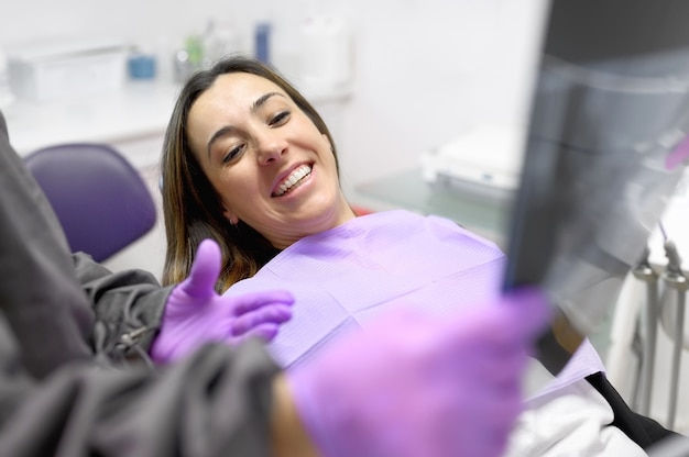 Dentista feminino apontando para a imagem de raio-x do paciente no consultório odontológico.