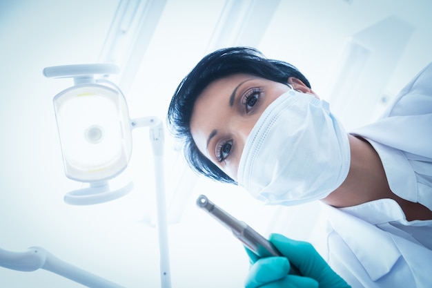 Dentista feminino em máscara cirúrgica segurando broca dental