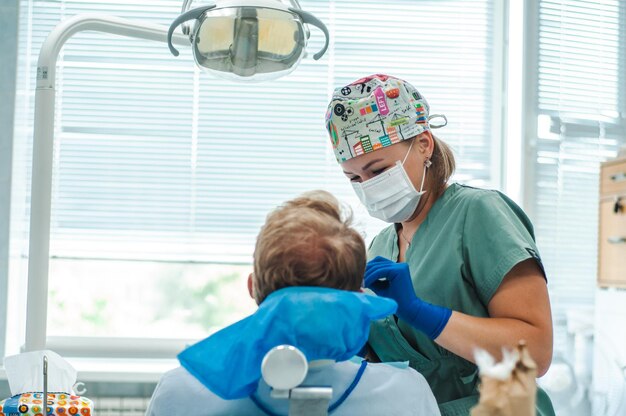 dentista feminino em máscara de luvas e boné com ferramentas nas mãos o paciente encontra-se na cadeira de tratamento