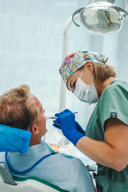 dentista feminino em máscara de luvas e boné com ferramentas nas mãos o paciente encontra-se na cadeira de tratamento