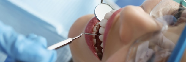 Dentista en guantes protectores examinando los dientes de la paciente con instrumentos metálicos en la clínica clo ...