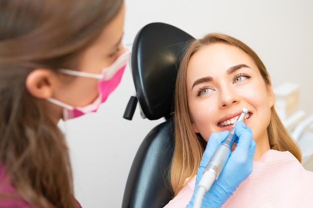 Un dentista haciendo cuidadosamente un procedimiento de molienda de dientes a una mujer graciosa mejorando la estética de