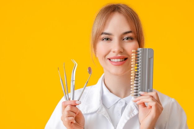 Dentista con herramientas y carta de colores de dientes en superficie amarilla