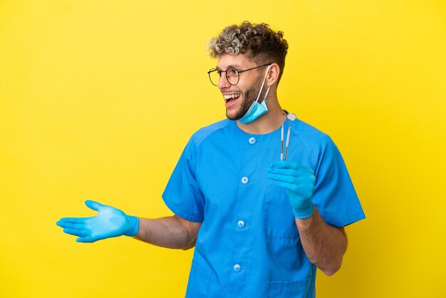 Dentista hombre caucásico sosteniendo herramientas aisladas sobre fondo amarillo con expresión de sorpresa mientras mira de lado