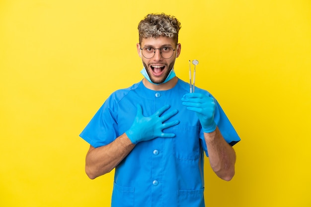 Dentista hombre caucásico sosteniendo herramientas aisladas sobre fondo amarillo sorprendido y conmocionado mientras mira a la derecha