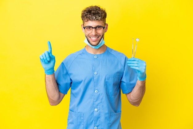 Dentista hombre rubio sosteniendo herramientas aisladas en el fondo apuntando a una gran idea