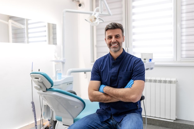 Dentista hombre sonriendo mientras está de pie en la clínica dental Retrato de un joven dentista confiado que trabaja en su sala de consulta