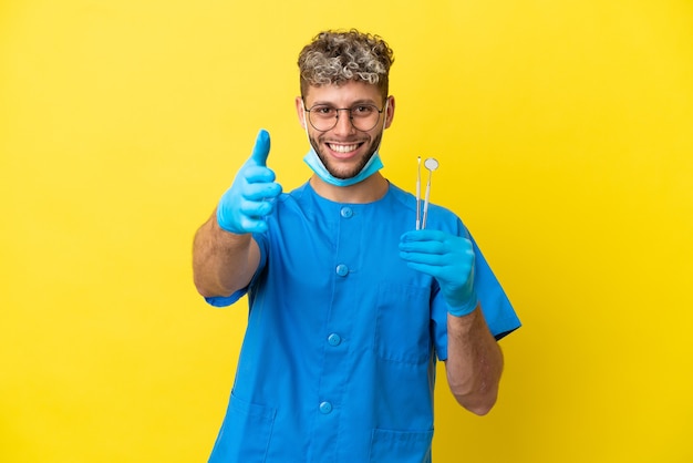 Dentista, homem caucasiano, segurando ferramentas isoladas em um fundo amarelo, apertando as mãos para fechar um bom negócio