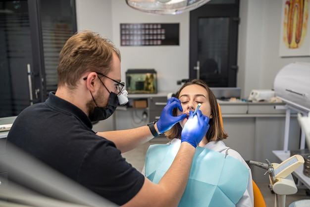 Dentista humano está operando uma jovem sorridente em uma clínica odontológica