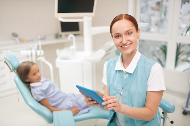 Dentista infantil sonriendo. Radiante dentista niño hermoso vistiendo uniforme sonriendo antes del examen