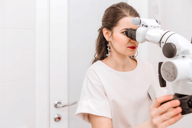 Dentista jovem atraente em um terno branco usando um microscópio