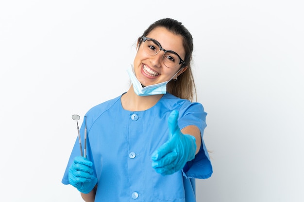 Dentista jovem segurando ferramentas isoladas na parede branca, apertando as mãos para fechar um bom negócio