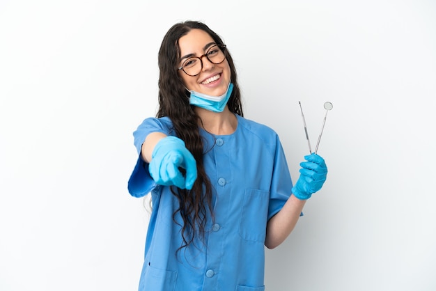 Dentista jovem segurando ferramentas isoladas na parede branca e apontando para a frente com uma expressão feliz