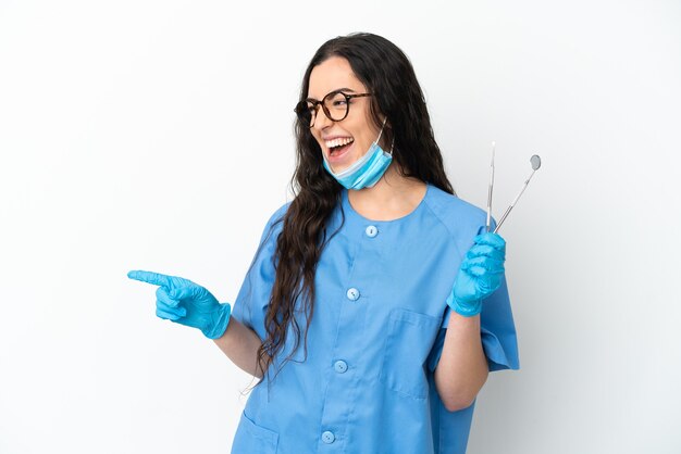 Dentista jovem segurando ferramentas isoladas no fundo branco, apontando o dedo para o lado e apresentando um produto