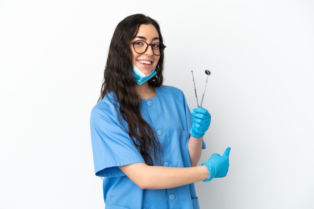 Dentista jovem segurando ferramentas isoladas no fundo branco apontando para trás