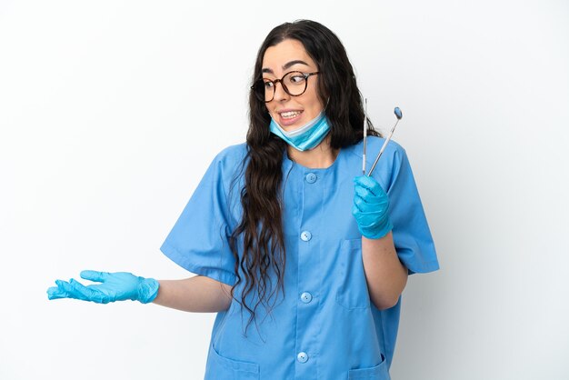 Dentista jovem segurando ferramentas isoladas no fundo branco com expressão de surpresa enquanto olha para o lado