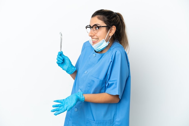 Dentista jovem segurando ferramentas isoladas no fundo branco com expressão de surpresa enquanto olha para o lado