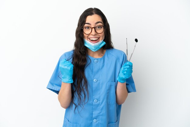 Dentista jovem segurando ferramentas isoladas no fundo branco, comemorando a vitória na posição vencedora