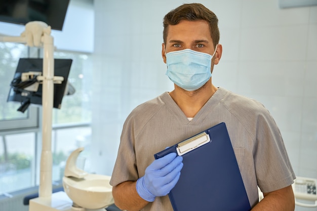 Dentista joven atractivo posando junto a la silla dental