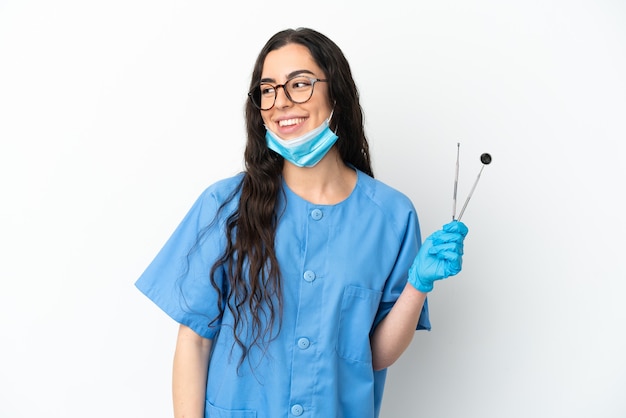 Dentista joven sosteniendo herramientas aisladas mirando hacia el lado y sonriendo