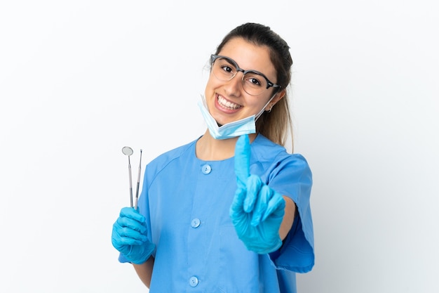 Dentista joven sosteniendo herramientas aisladas sobre fondo blanco mostrando y levantando un dedo
