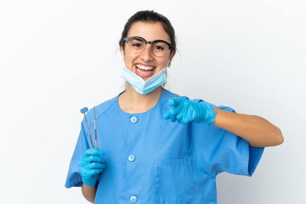 Dentista joven sosteniendo herramientas aisladas sobre fondo blanco sorprendido y apuntando hacia el frente