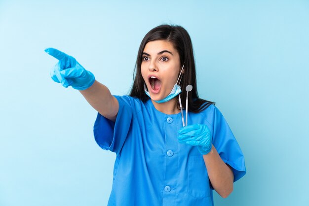 Dentista joven sosteniendo herramientas sobre azul aislado apuntando hacia afuera