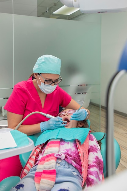 Dentista limpando os dentes de uma menina deitada na cadeira no consultório dentário