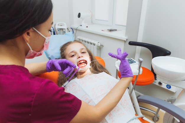 El dentista limpia los dientes de una niña con hilo dental Foto de un paciente con la boca abierta con un dique de goma