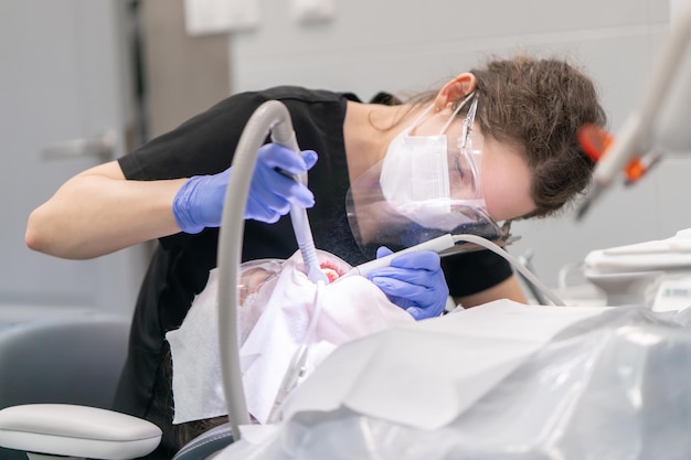 Un dentista limpia los dientes de placa y sarro usando un dispositivo de abrasión de aire