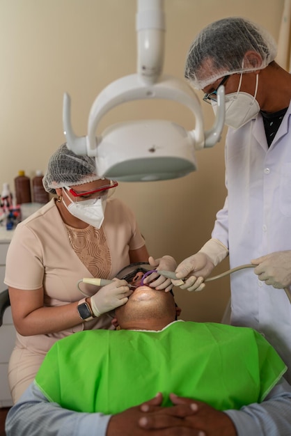 Dentista limpiando los dientes de un paciente usando una herramienta dental eléctrica