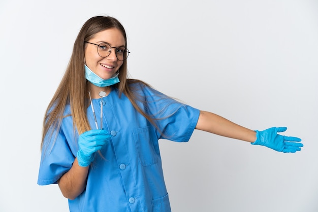 Dentista lituana segurando ferramentas sobre um fundo isolado, estendendo as mãos para o lado para convidar para vir