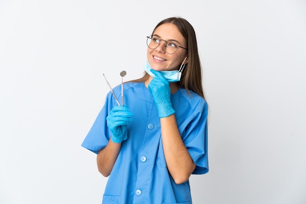 Dentista lituana segurando ferramentas sobre uma parede isolada, olhando para cima enquanto sorri