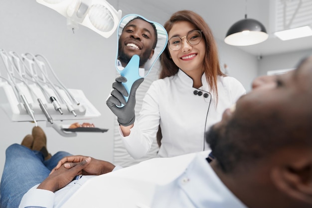 Dentista mantendo espelho e mostrando sorriso branco ao paciente