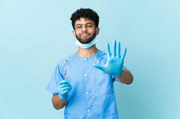 Dentista marroquí hombre sujetando herramientas en azul contando cinco con los dedos