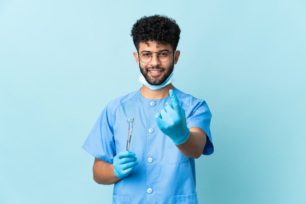 Dentista marroquí hombre sujetando herramientas en azul haciendo gesto que viene