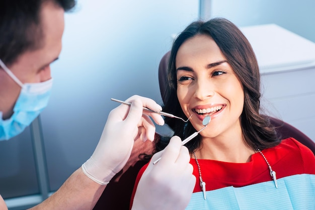 El dentista en la máscara facial y los guantes del bucle del oído sostiene los instrumentos dentales y comprueba el resultado de su trabajo profesional en el centro dental