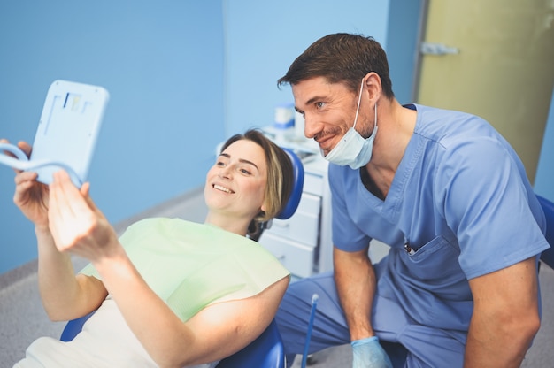 Dentista masculina mostra a paciente feliz os resultados do tratamento com um espelho no consultório odontológico
