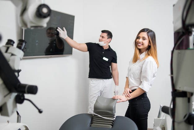 Dentista masculina, mostrando ao paciente do sexo feminino sua imagem de raio-x dental na tela do computador no consultório odontológico