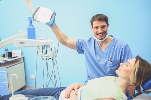 Dentista masculina que examina os dentes de um paciente usando equipamento dental no consultório odontológico