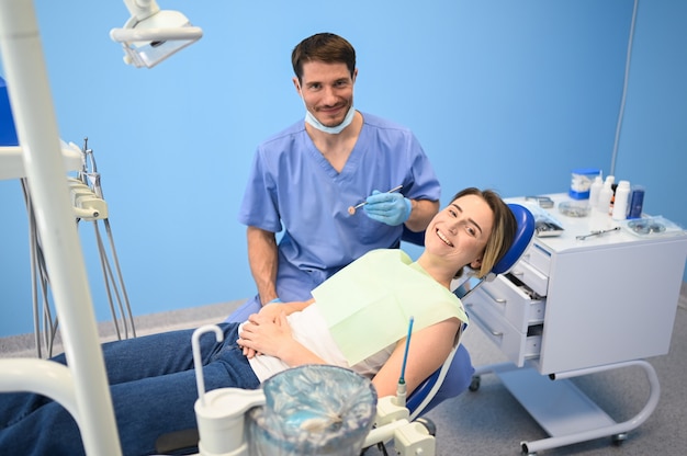 Dentista masculino examinando los dientes de un paciente usando equipo dental en la oficina de odontología