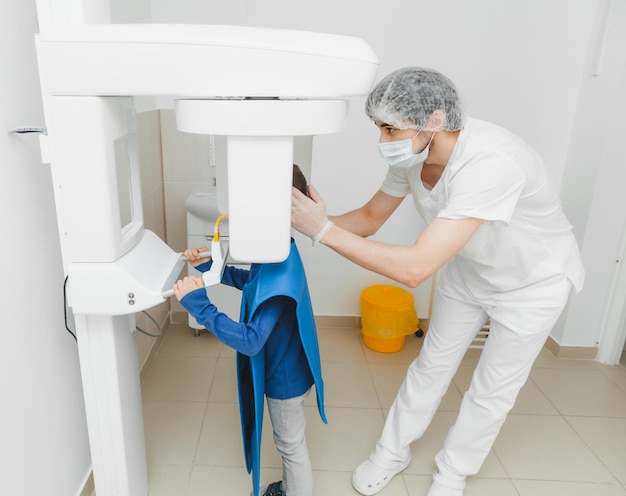 Un dentista masculino hace una radiografía panorámica de los dientes de un niño usando una máquina de rayos X moderna