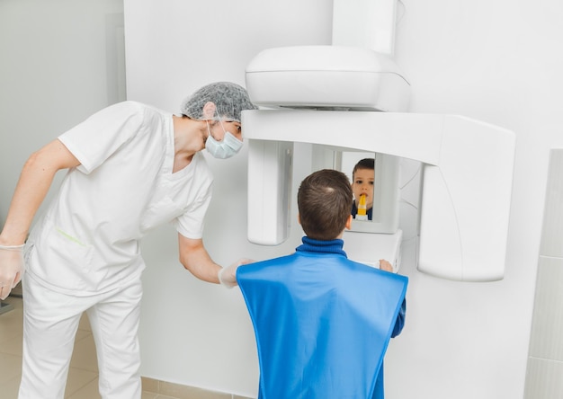 Un dentista masculino hace una radiografía panorámica de los dientes de un niño usando una máquina de rayos X moderna