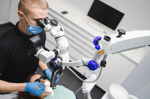 Dentista masculino jovem profissional usa um microscópio para tratar uma paciente do sexo feminino