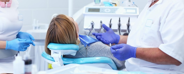 Foto dentista masculino mayor en el consultorio dental hablando con una paciente y preparándose para el tratamiento